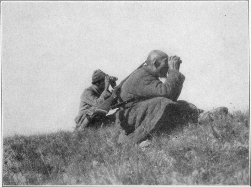 Two men crouching while looking through binoculars.