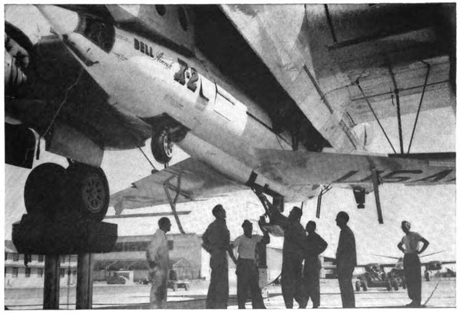 Several men looking up at a plane mounted underneath a larger plane