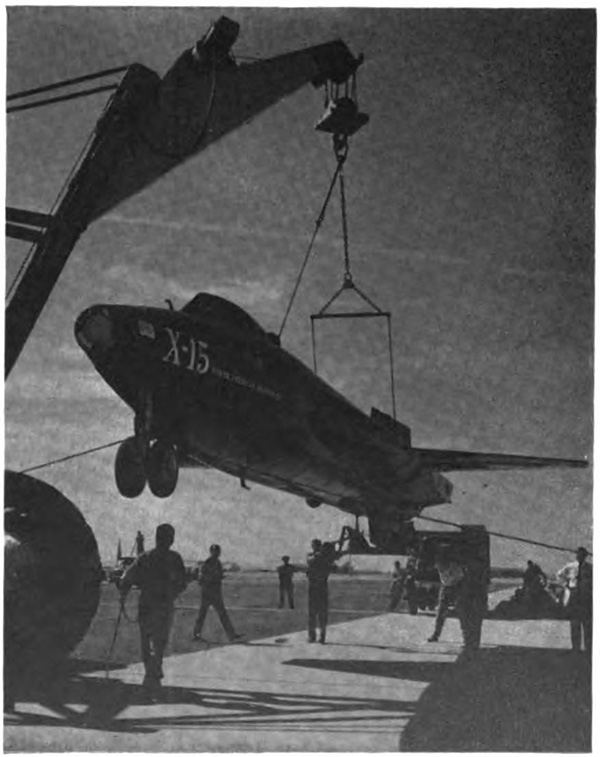 An aircraft hanging in mid-air from a crane with several people surrounding it