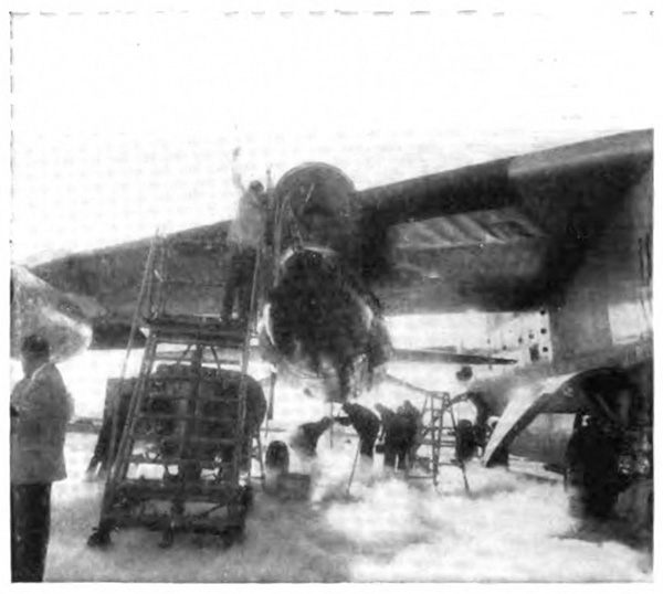 A groups of people surrounding a small plane attached to a larger plane, one on a ladder