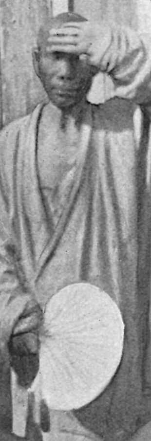 Monk covering forehead with left hand, holding a fan with his right