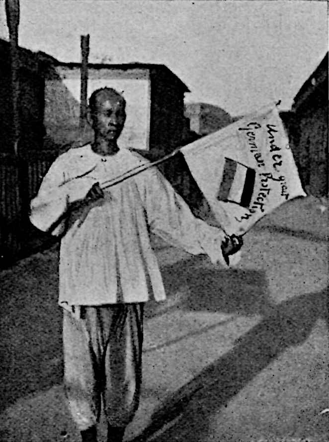 Man holding white flag that has a tri-color flag with text: Under great German Protection; great uncertain